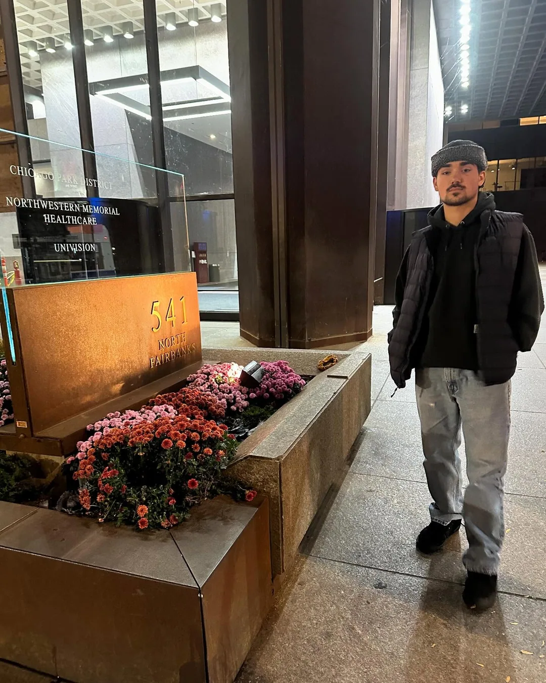 Alex outside a Chicago building, in a black vest and gray trousers.