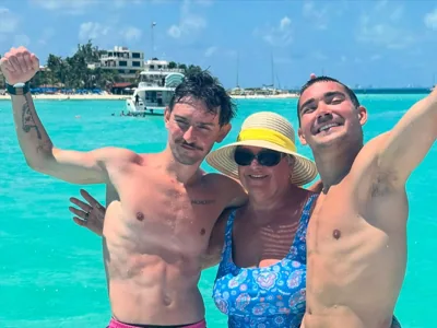 Three people smiling together beside turquoise water.