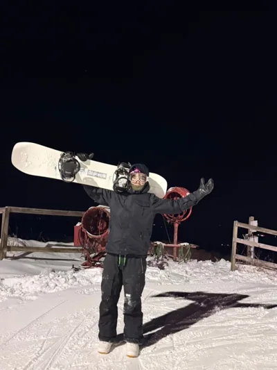 Alex holding a snowboard overhead under lights at night.