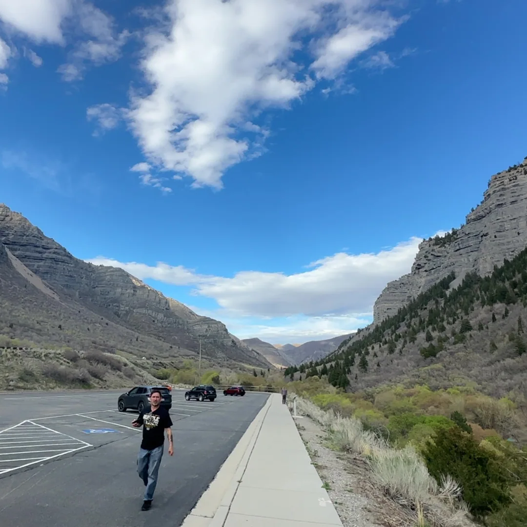 A person standing in a parking area between rocky mountains.