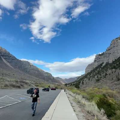 A person standing in a parking area between rocky mountains.