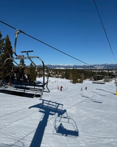 Chairlifts, trees, and snow under a bright sky.