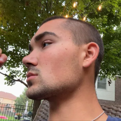 A side-profile portrait outdoors beneath leaves and lights.