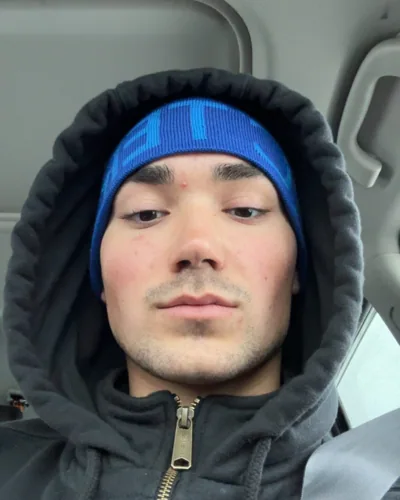 A close portrait in a blue beanie and dark hood.
