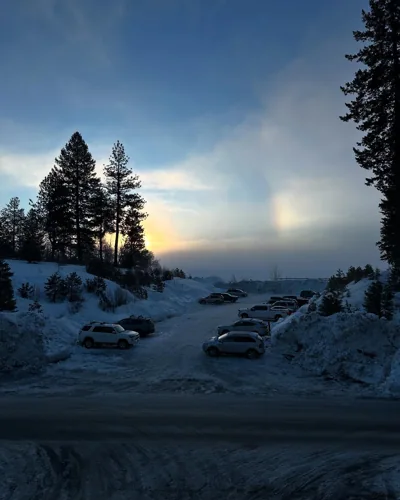 A winter sunset above trees and a snow-covered parking area.