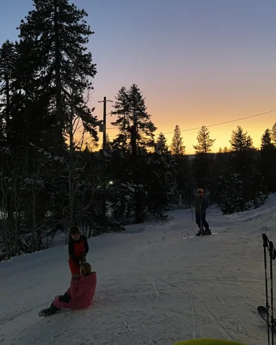 Riders resting on snow as the sky turns orange.