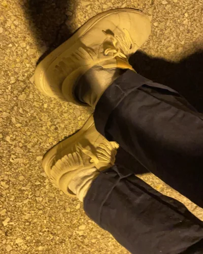 A close photograph of shoes and trousers under yellow street light.