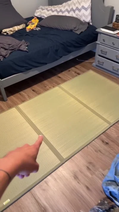 A floor mat on the wood floor beside a bed.
